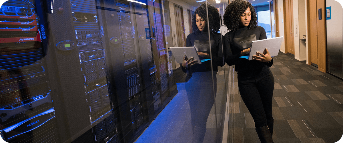 IT professional reviewing a tablet beside a glass-walled datacenter with illuminated server racks