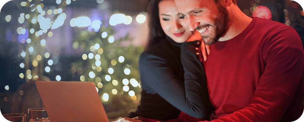 Couple smiling together while looking at a laptop in a warm cafe setting