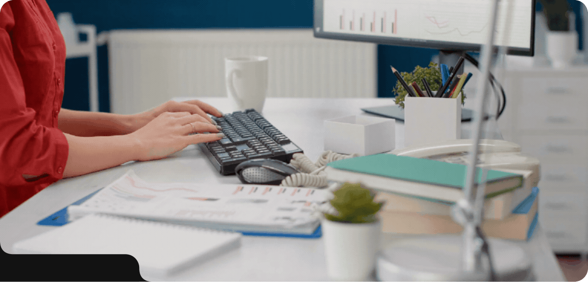 Person typing on a keyboard with analytics charts on a monitor in a modern office