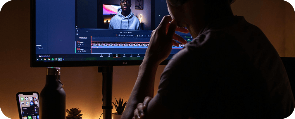 Video editor working on a large monitor in a dimly lit creative studio