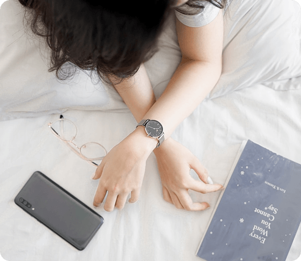 Person resting in bed with a smartphone and watch nearby