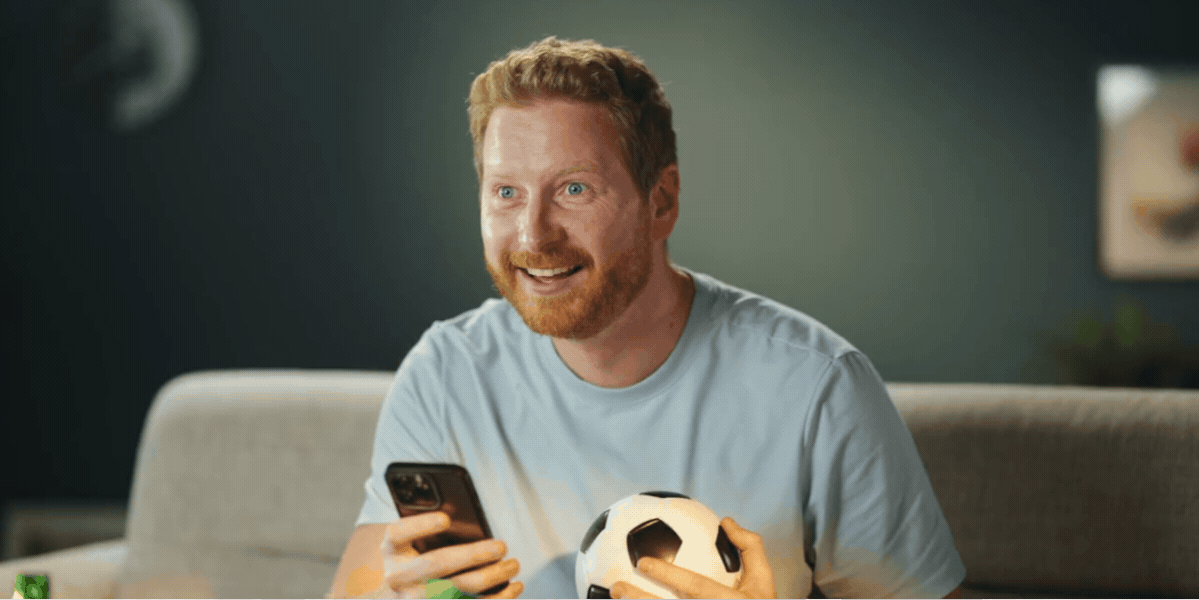 Enthusiastic fantasy sports fan holding a smartphone and soccer ball