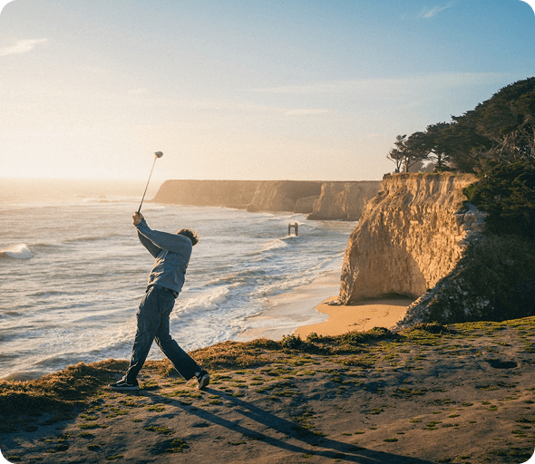 Golfer swinging on a coastal cliff course at sunset