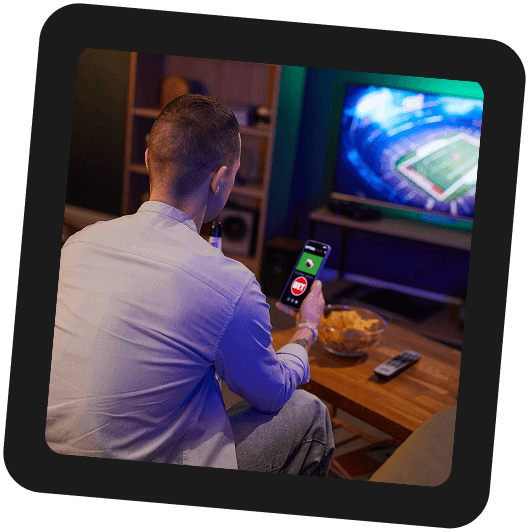 Fan watching a football game on TV while using a fantasy sports app on a phone