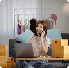 Entrepreneur managing ecommerce orders on a phone among shipping boxes