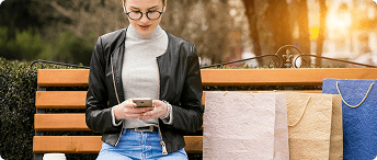 Woman shopping on a smartphone while sitting on a park bench