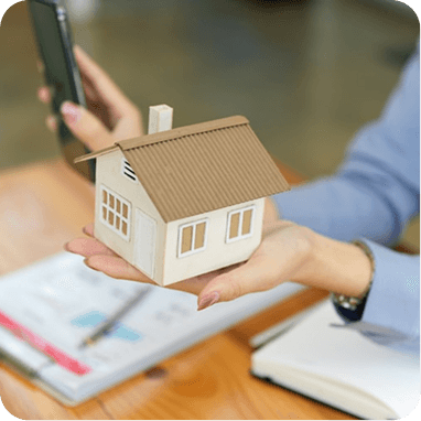 Hands holding a model house above documents and a smartphone