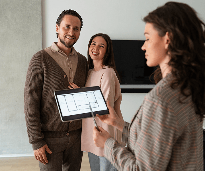 Real estate agent showing a floor plan on a tablet to a couple