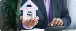 Professional holding a model house while using a calculator