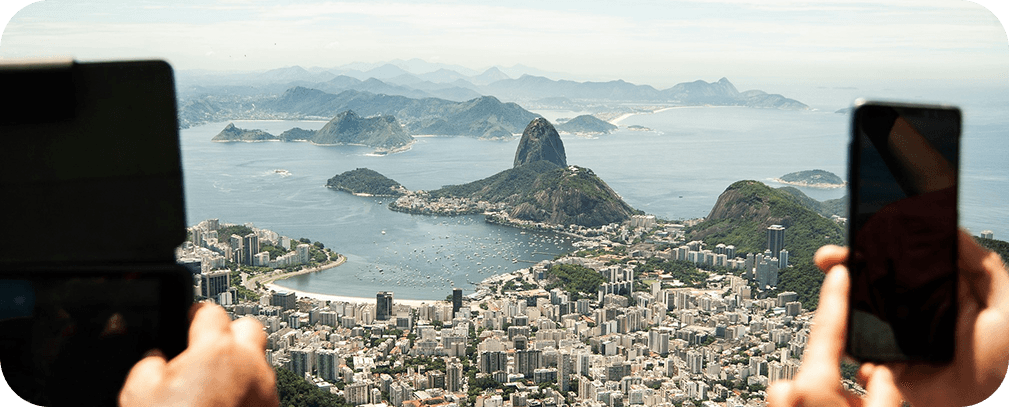 Hands holding smartphones capturing a panoramic coastal city landscape