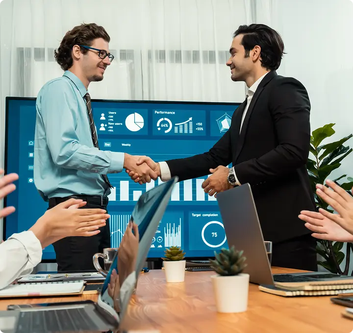 Business partners shaking hands in front of a performance dashboard