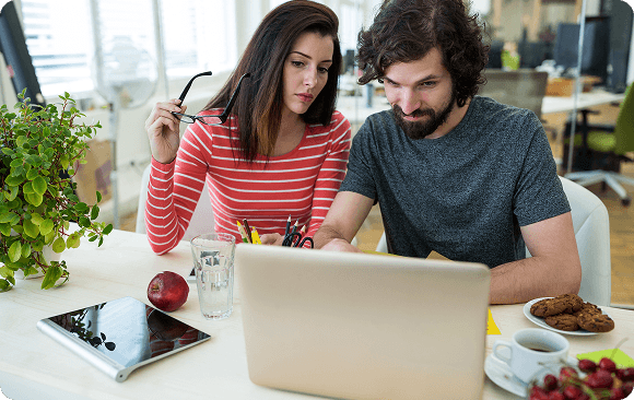 Man and woman collaborating at a desk while reviewing a laptop