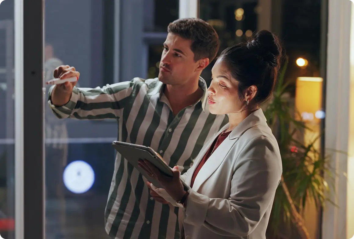 Consultants mapping a plan on a glass board while reviewing a tablet